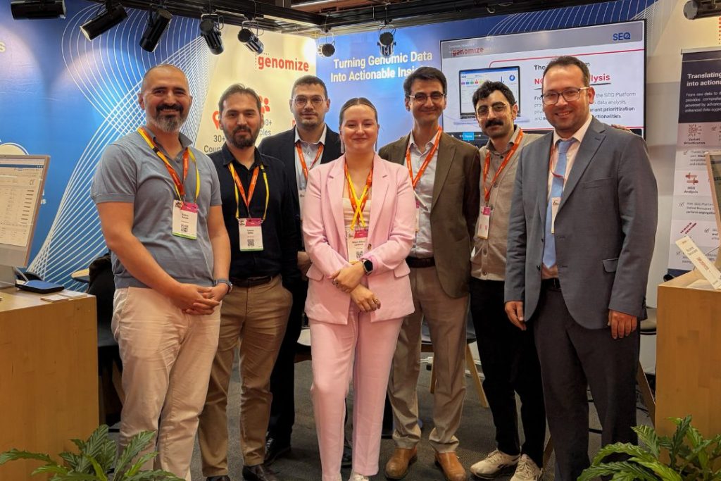 Group photo of the Genomize team at their conference booth, standing in front of SEQ Platform displays and genomic analysis presentations during a genomics event.