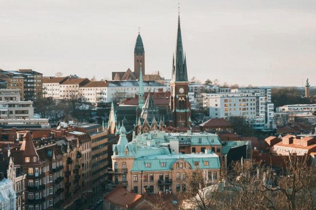 gothenburg Aerial view of Gothenburg, Sweden, featuring historic church spires, red-roofed buildings, and a mix of classic and modern architecture. The cityscape highlights prominent landmarks rising above the urban skyline, with residential and commercial buildings extending into the distance. This image captures the character of Gothenburg, the host city of the European Human Genetics Conference (ESHG 2026).